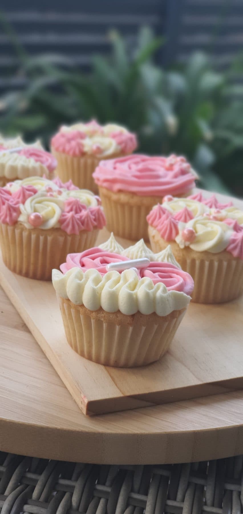 Cupcakes decorados con frosting rosa y blanco sobre tabla de madera