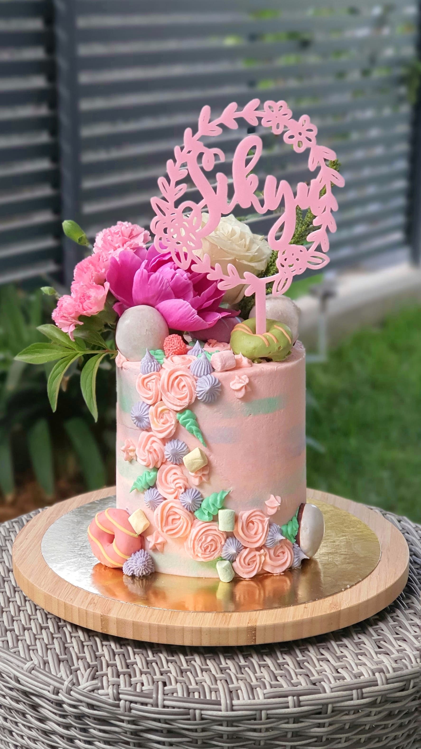 Tarta alta rosa con flores, macarons y topper Sikyu sobre pedestal de madera